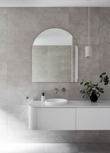 Modern bathroom with arched mirror, floating white vanity, and gray tile walls.