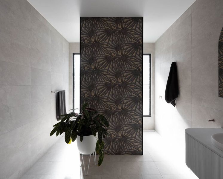 A modern bathroom with a patterned panel, featuring a plant, towels, and neutral-toned walls.