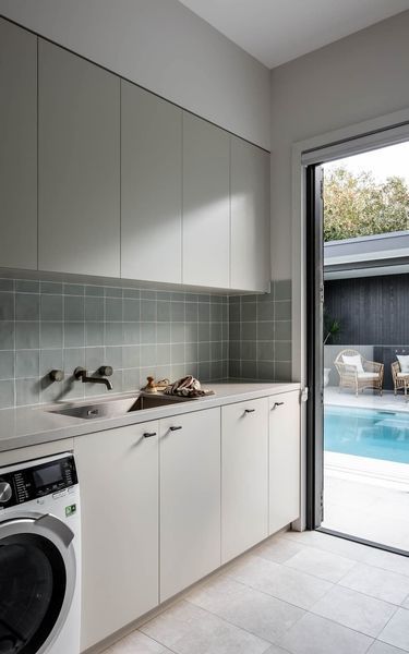 Laundry room with light gray cabinets, blue-green backsplash, and open door to a pool area.