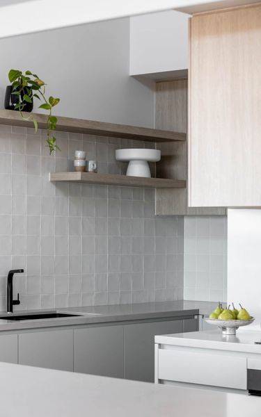 Modern kitchen with gray countertop, shelves, and cabinetry, with a black faucet and a small cake stand.