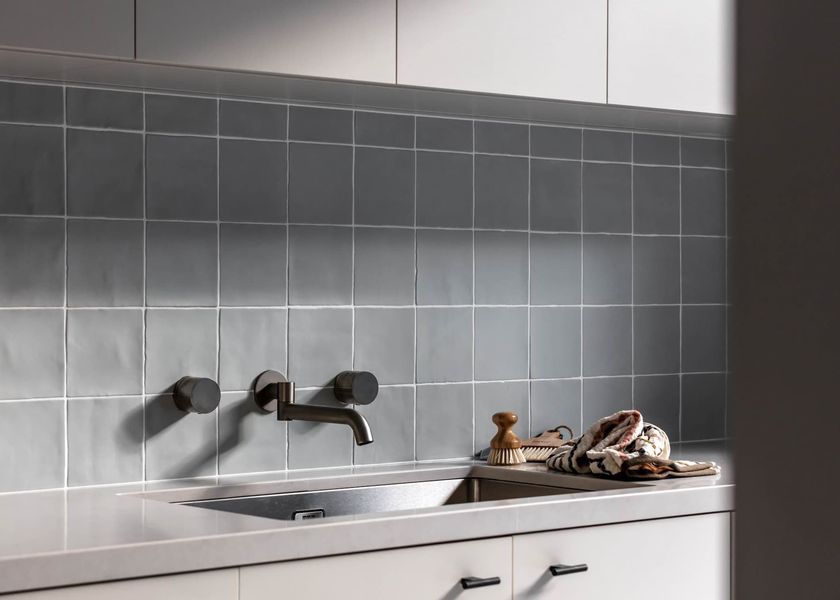 Kitchen backsplash with gray square tiles and a faucet over a sink.