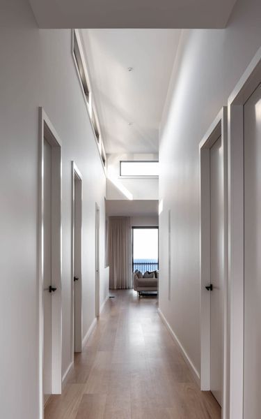 Long, white hallway with doors on both sides, leading to a room with a window.