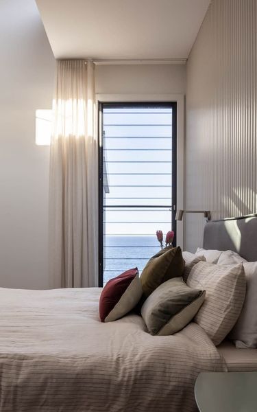 Bedroom with bed, colorful pillows, and a view of the ocean through the door.