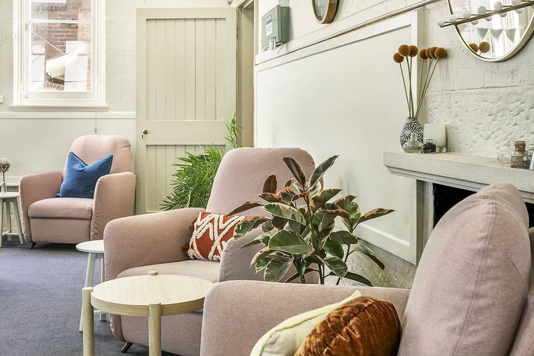 Cozy waiting room with pink armchairs, small side tables, plants, and a fireplace.