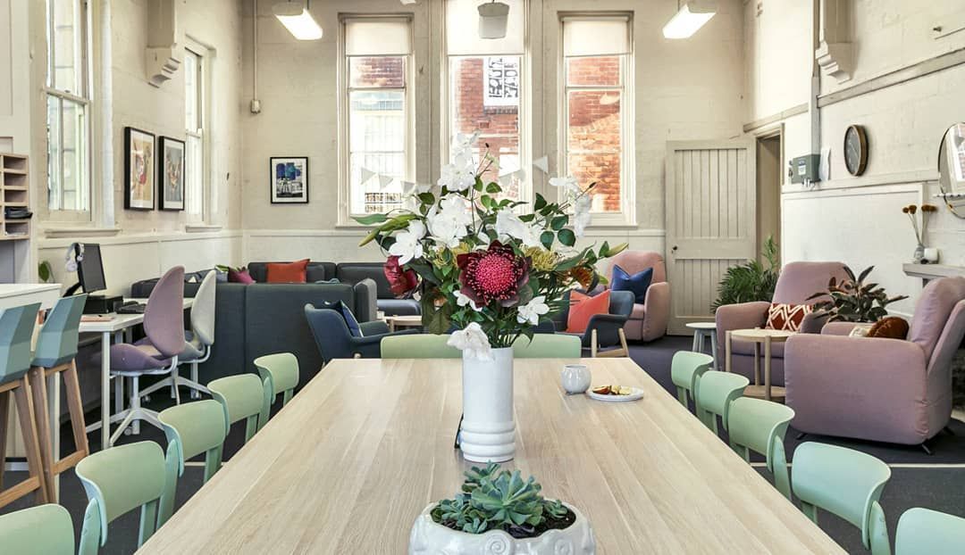 Long wooden table with flower arrangement, facing comfortable seating area in a bright, open room.