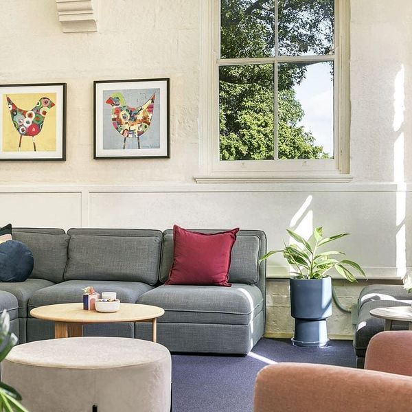 A cozy lounge with a gray sectional sofa, colorful artwork, and a large window overlooking greenery.