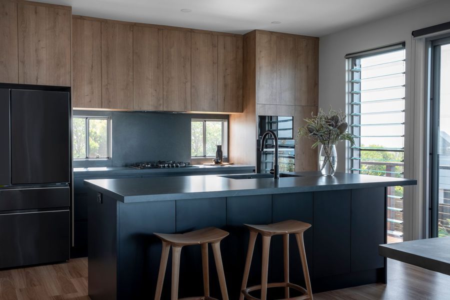 Modern kitchen with dark blue island, wooden cabinets, and black refrigerator.