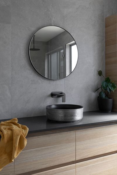 Bathroom with round mirror, gray sink, wooden cabinets, and a green plant.