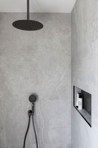 Modern gray tiled shower with black showerhead and handheld. Built-in shelf holds toiletries.