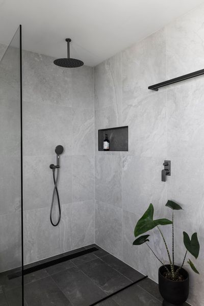 Modern gray tiled shower with black fixtures and plant.