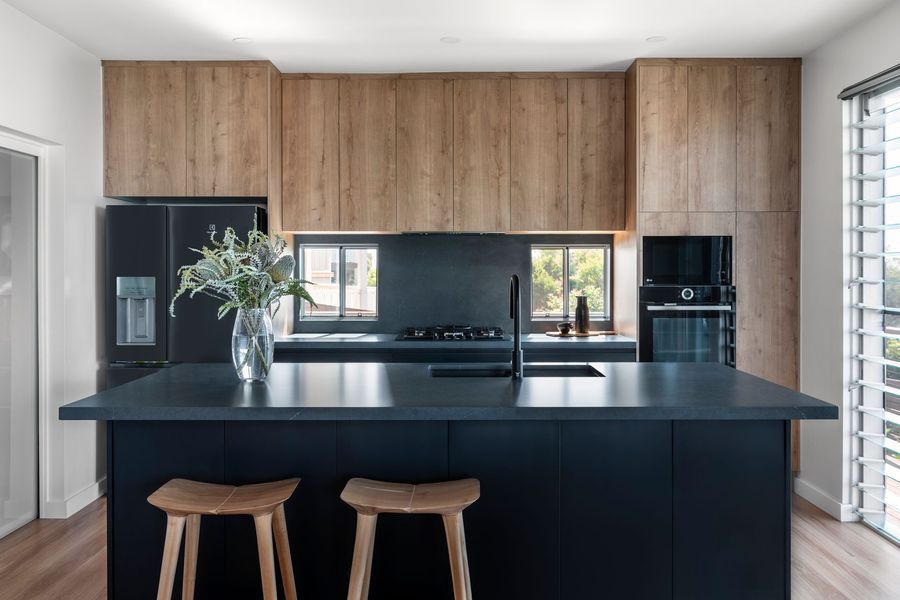 Modern kitchen with a black island, wooden cabinets, and two wooden stools.