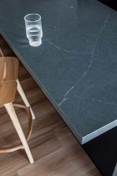 A close-up of a gray countertop with a glass of water and a wooden stool.