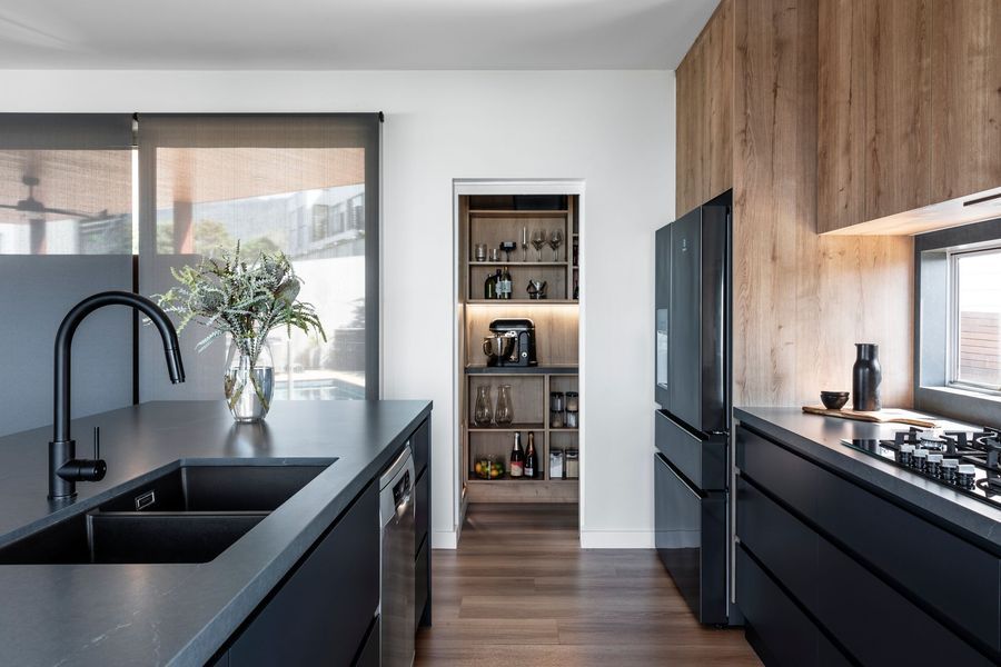 Modern kitchen with black cabinets, wood paneling, and walk-in pantry.