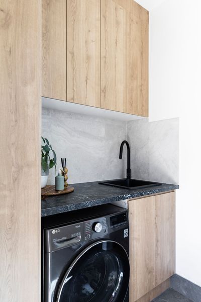 Laundry room with black washer, sink, and light wood cabinets.