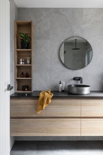 Bathroom with wooden vanity, gray walls, round mirror, and open shelf.