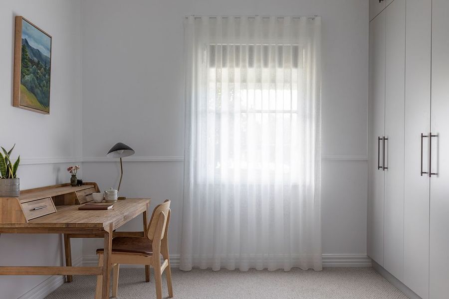 White room with desk, chair, and sheer curtains over a window. Built-in wardrobe on the right.