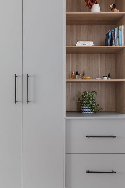 Gray wardrobe with open shelving and drawers; interior with books, plants, and toiletries.