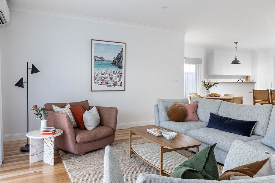 Living room with a corner sofa, armchair, coffee table, and artwork; open to a kitchen.