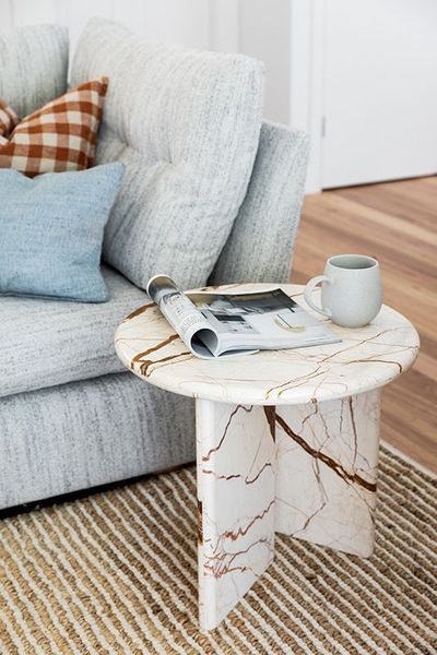 Marble side table next to a light blue couch, with a magazine and mug on top.