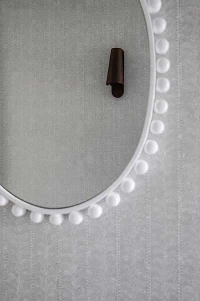 White pompom-trimmed mirror on textured gray wall; brown wall hook.
