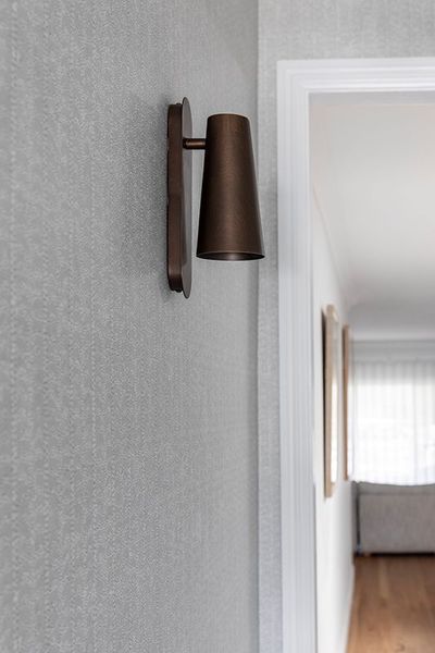 Bronze wall sconce on a textured gray wall, next to a doorway to a light-filled room.