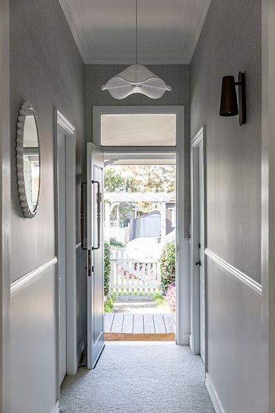Hallway with light gray walls, open door to a backyard, and a round mirror.
