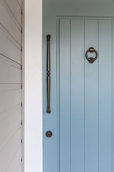 Blue door with black handle and knocker. White wall on the left.