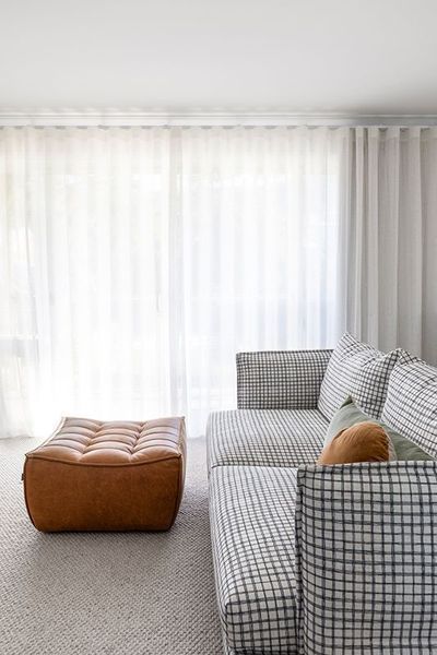 Tan leather ottoman and patterned sofa in front of sheer white curtains.