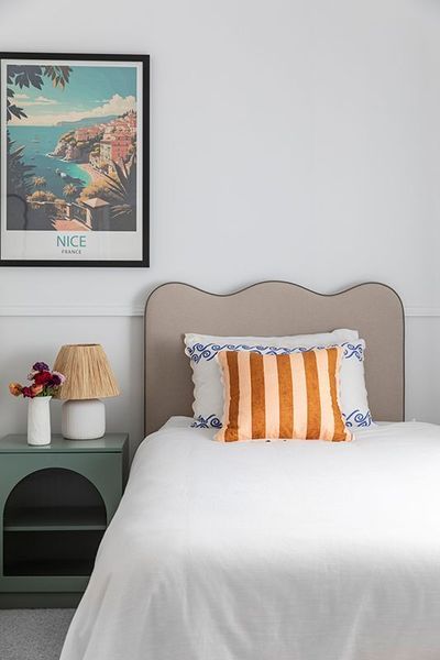 Bedroom with a scalloped headboard, striped orange pillow, artwork, and a green nightstand.