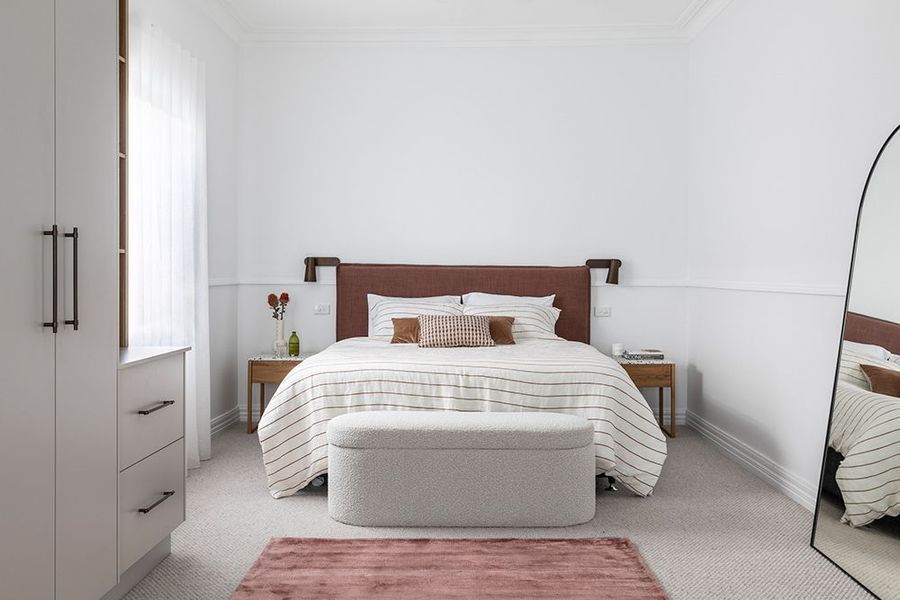 Bedroom with a bed, wardrobe, and mirror. White walls, brown headboard, and pink rug.