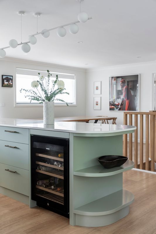 Light green kitchen island with wine fridge and open shelving; vase of flowers on the countertop.