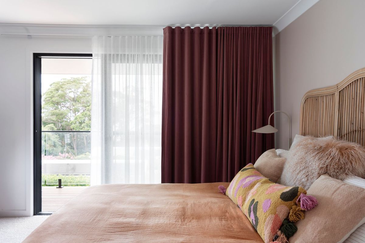Bedroom with a burgundy curtain, sheer white curtain, and a bed with pillows.