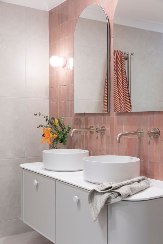 A modern bathroom with pink tile, white sinks, and a white vanity.