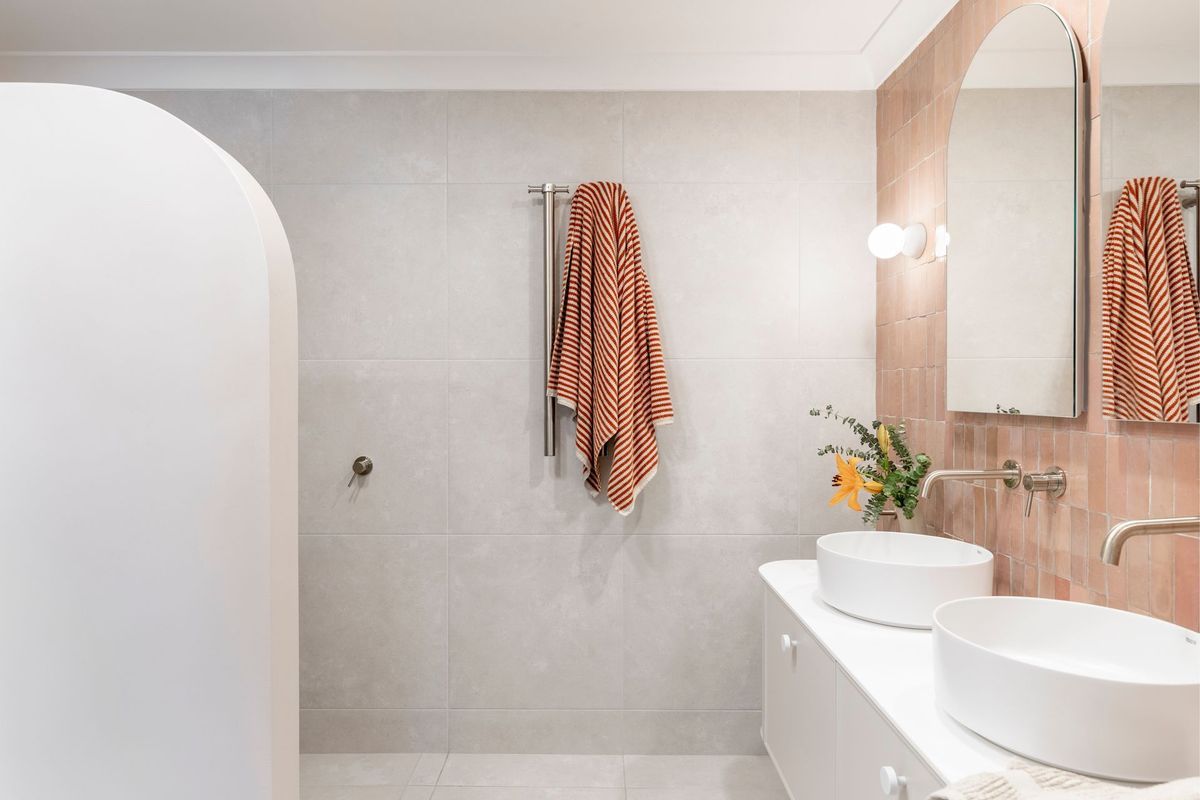Modern bathroom with light gray walls, white sinks, and a warm orange towel.