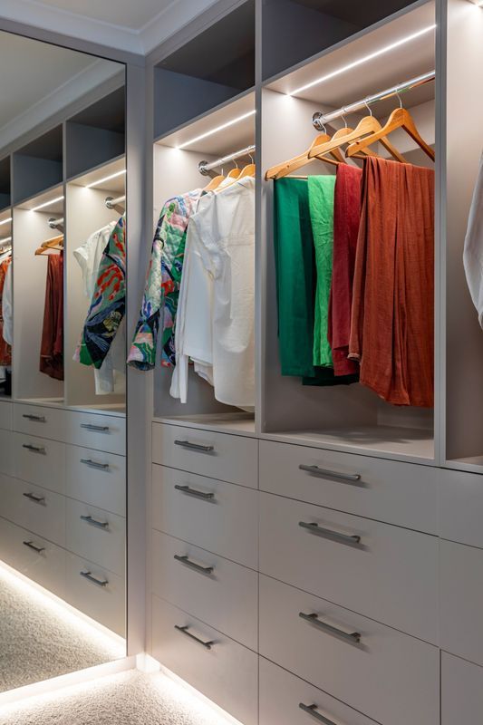 Walk-in closet with gray cabinets, hanging clothes, drawers, and LED lighting.