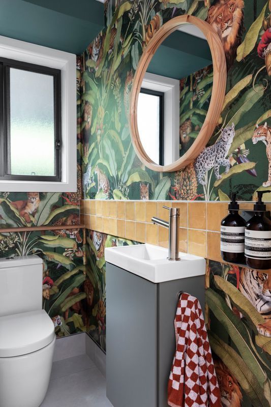 Small bathroom with jungle-themed wallpaper, a gray sink cabinet, round mirror, and a white toilet.