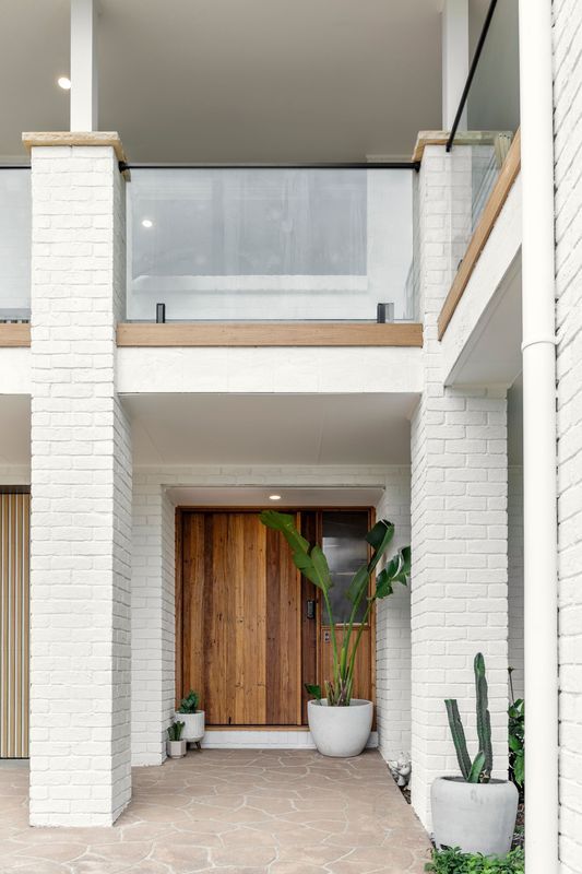 Exterior view of a modern home's entrance with a wooden door, white brick columns, and potted plants.