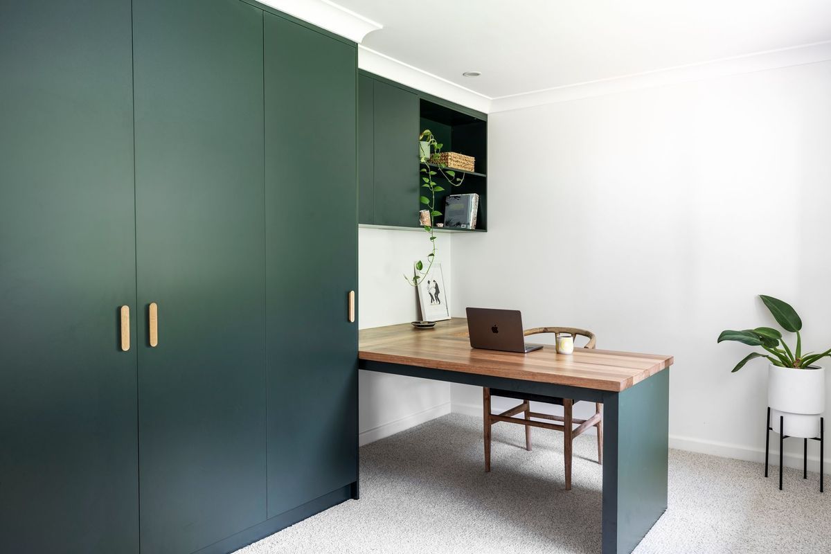 Dark green built-in office with wood desk, chair, and cabinets. Includes a potted plant and a laptop.