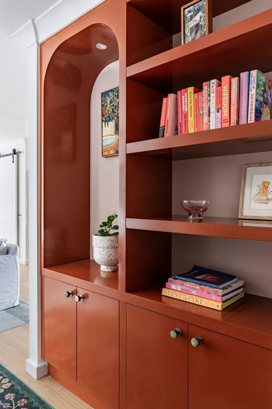 Built-in orange bookcase with arched niche, filled with books and decor, against a white wall.
