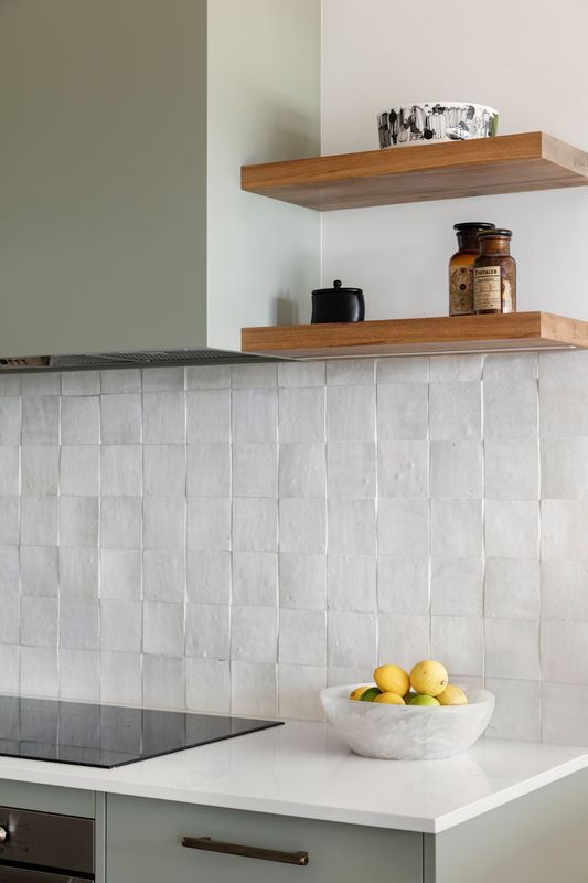 Kitchen with white square tile backsplash, wooden shelves, and a bowl of lemons.