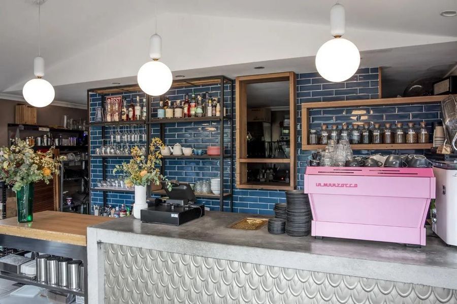 Coffee shop interior with blue tiled walls, a pink espresso machine, and globe lights.