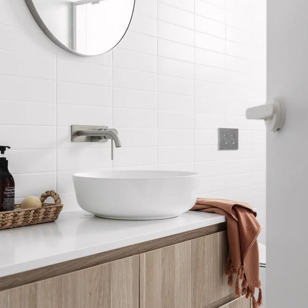 White bathroom with vessel sink, light wood vanity, and white tiled walls.