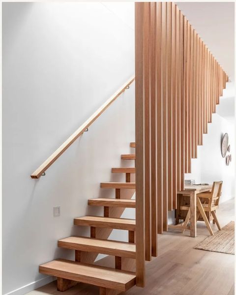 Wooden staircase with a vertical slat wood railing and a wooden handrail on a white wall.