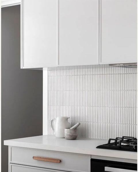 White kitchen with vertically-stacked, narrow tiles. White cabinets, countertop, and pitcher.