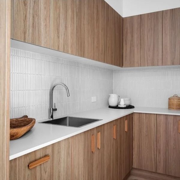 Modern kitchen with light wood cabinets, white countertop, and a stainless steel sink.