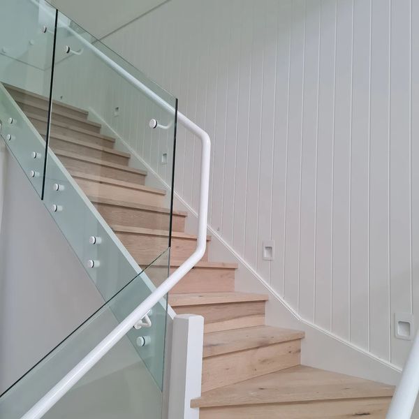 Staircase with wooden steps, glass panels, and white handrails against a white-paneled wall.