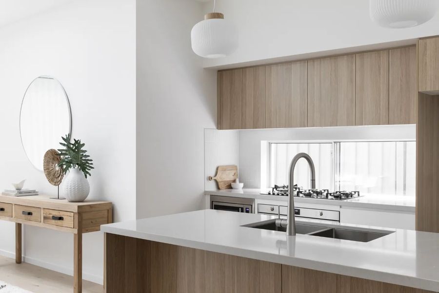Modern kitchen with light wood cabinetry, white countertops, and a stainless steel sink.
