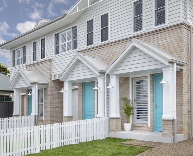 Row of townhouses with white picket fence, blue doors, and light grey brick exterior.