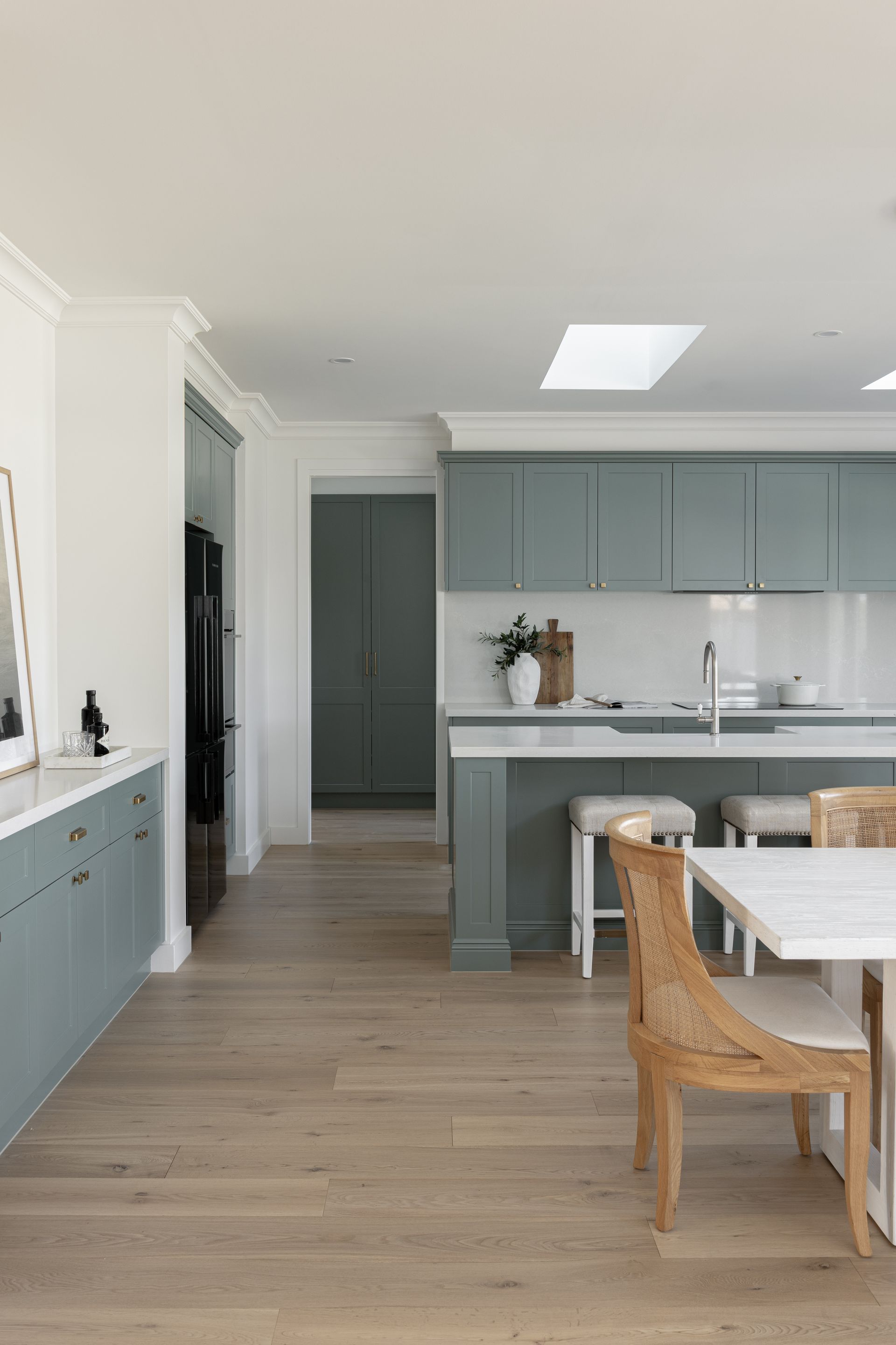 Spacious kitchen with teal cabinets, light wood floors, and a skylight. Dining table with rattan chairs.