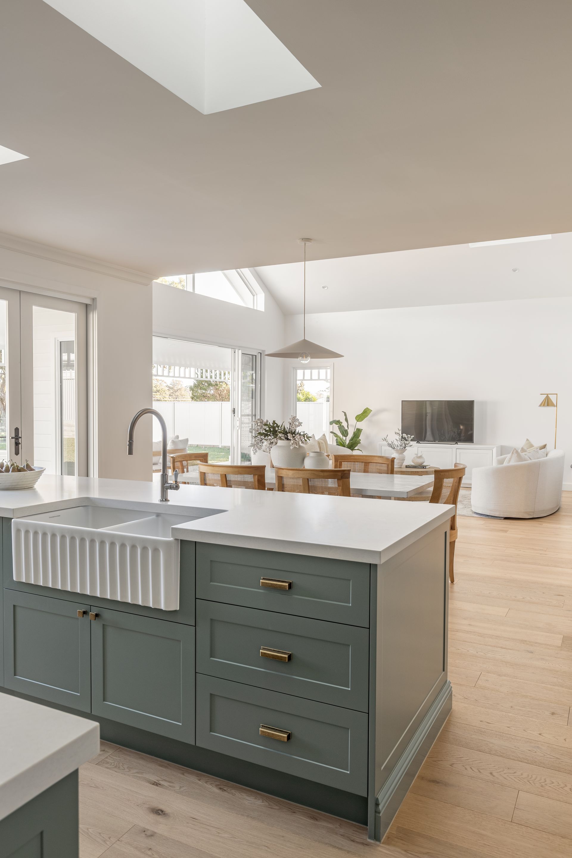 Kitchen island with farmhouse sink, green cabinets, white countertop; dining and living area visible.